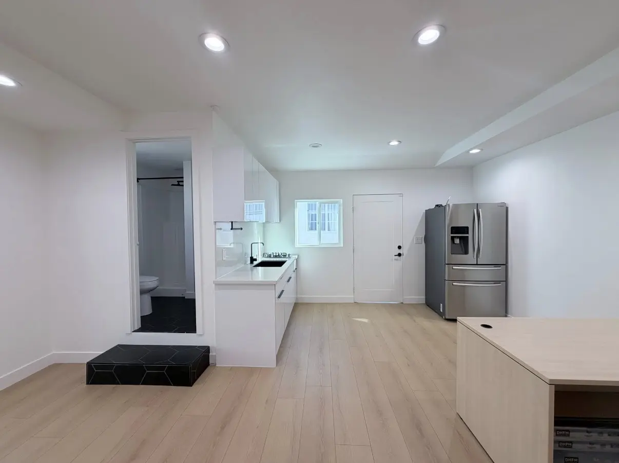 Bright open-plan kitchen with white flat-panel cabinetry, quartz-style counters, and light wide-plank flooring