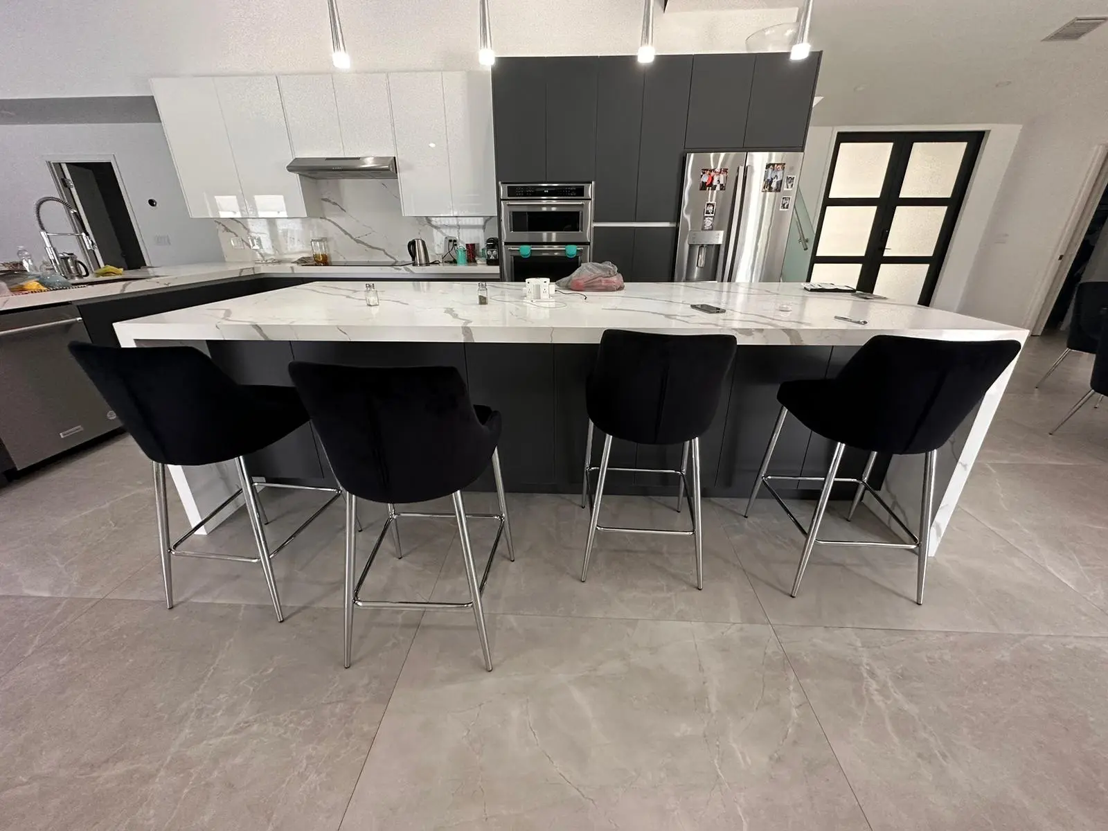 Completed kitchen with a veined waterfall island, black bar seating, and two-tone gray and white cabinetry