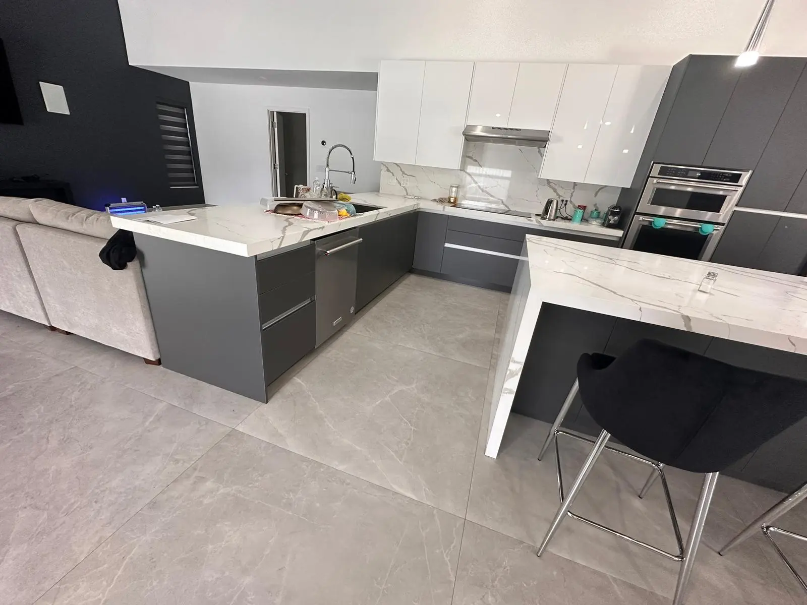 Completed kitchen remodel with gray flat-panel cabinetry, veined stone counters, and integrated wall ovens