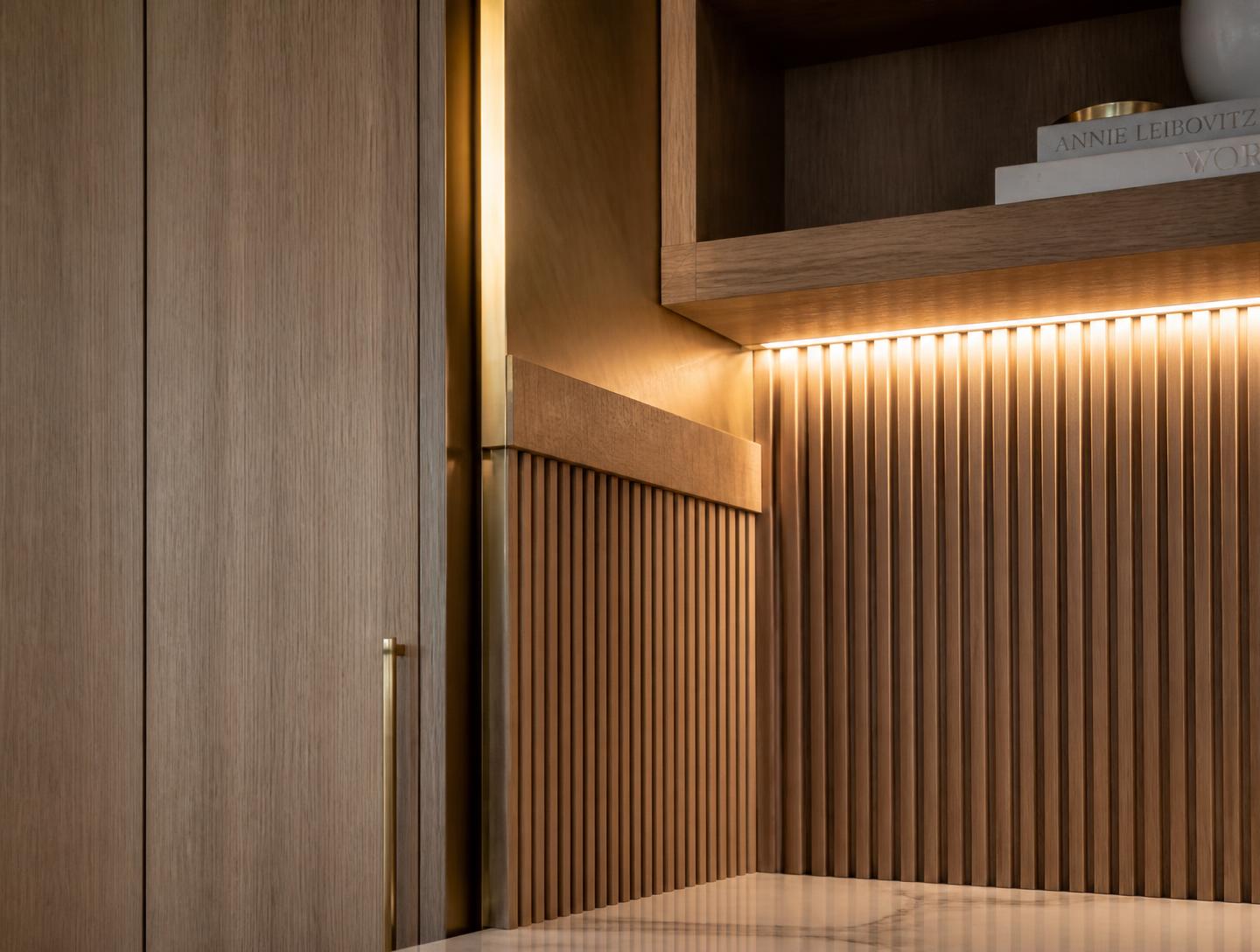 Detail of custom white oak millwork with brass reveal and integrated linear lighting